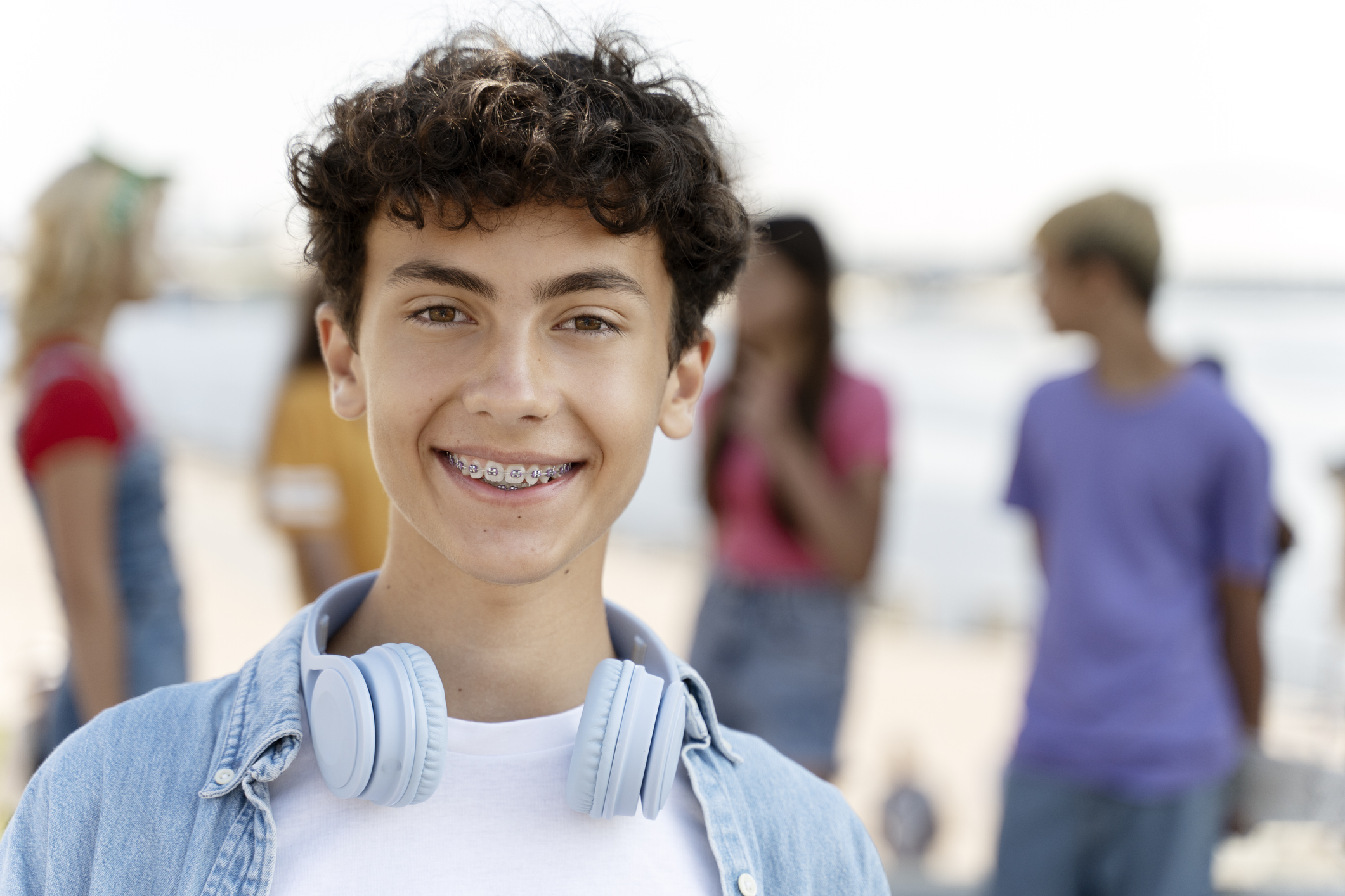 Affordable Braces with Dr. Wickson at SmileyVille - Portrait of smiling teenager with braces wearing headphones looking at camera standing on the street with friends on background. Summer concept