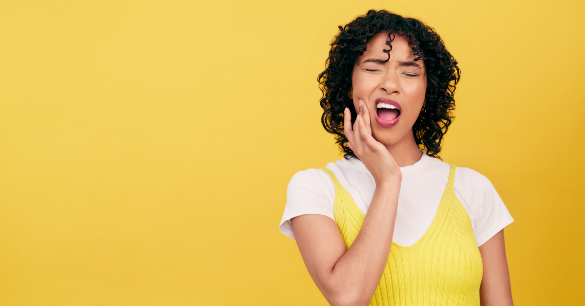 A woman with curly hair in a yellow top looks distressed with her eyes closed, holding her cheek, suggesting TMJ or toothache. Yellow background.