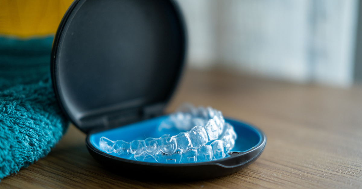 Clear dental aligners sit in an open black and blue case on a wooden surface. A teal towel is partially visible in the background, giving a tidy and sanitary tone.