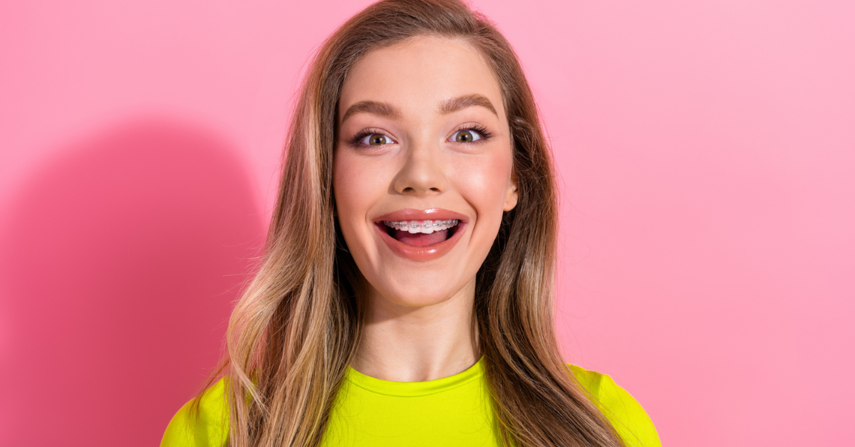 Smiling person with long hair and braces, wearing a bright yellow top. The pink background enhances the cheerful and vibrant mood of the image.