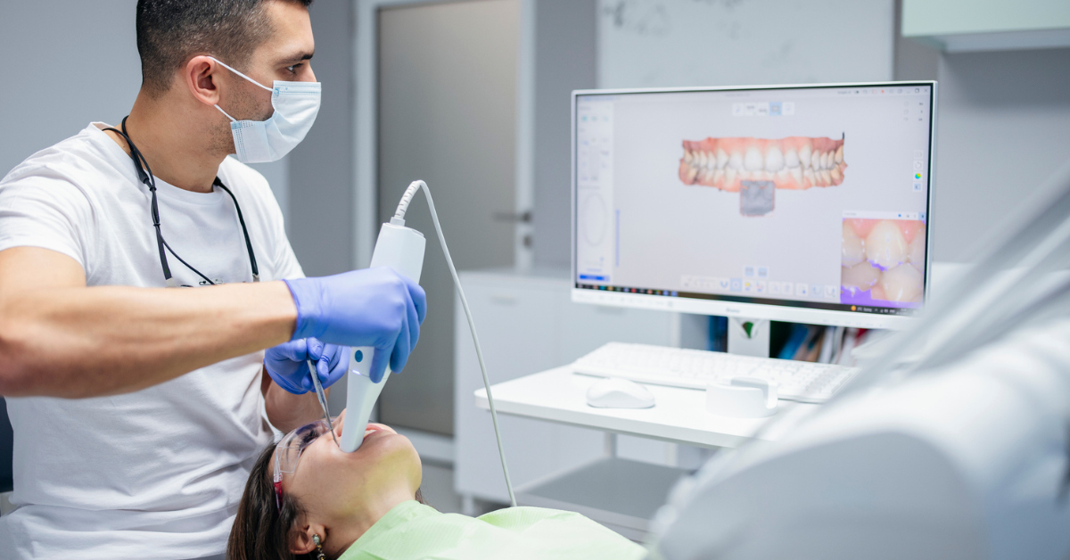 A dentist, wearing a mask and gloves, uses a digital scanner on a patient's teeth. A monitor beside them displays a 3D dental scan. The environment is clean and clinical.